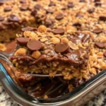 A freshly baked Peanut Butter Cup Dump Cake in a 9x13-inch baking dish, with a gooey chocolate and peanut butter swirl, topped with melted chocolate chips and mini peanut butter cups. The cake is slightly cracked on top, revealing its rich, warm texture, and is served with a scoop of vanilla ice cream on the side.