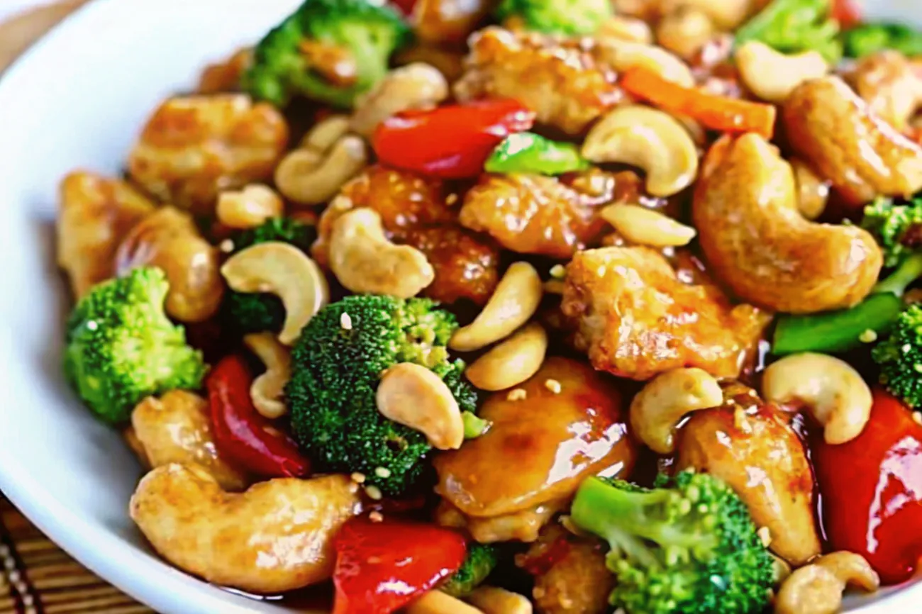 A plate of homemade cashew chicken garnished with green onions and cashews, served on a rustic wooden table with chopsticks.