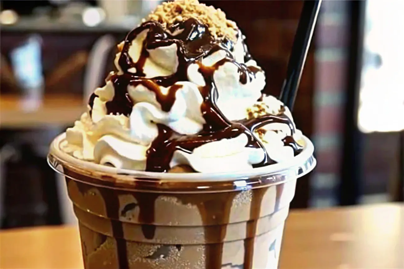 A delicious Reese’s Peanut Butter Frappuccino with chocolate drizzles and whipped cream, served in a tall glass.