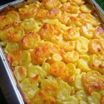 Golden scalloped potatoes in a baking dish, topped with melted cheddar cheese and paprika, garnished with fresh thyme, on a rustic wooden table.