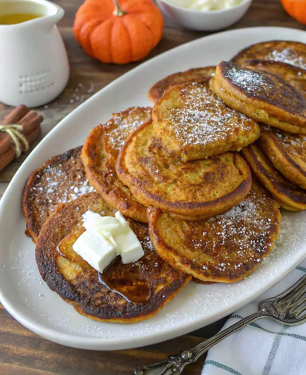 Stack of perfectly golden thick and flavorful pumpkin pancakes with maple syrup drizzle and autumn garnishes