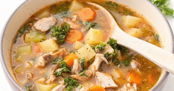 A steaming bowl of leftover chicken and potato soup garnished with fresh herbs, served with crusty bread on a rustic wooden table