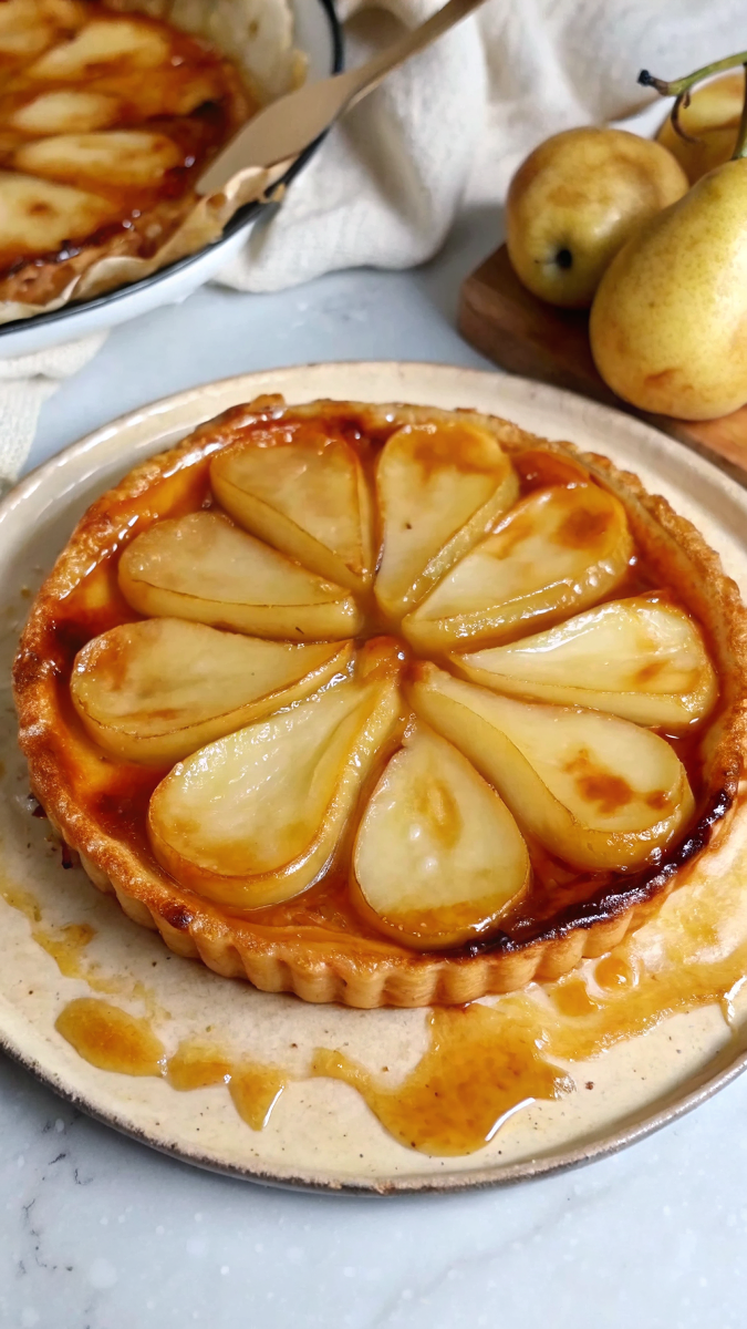 Beautiful finished Pear Tarte Tatin with golden caramelized pears and flaky pastry crust on white serving plate