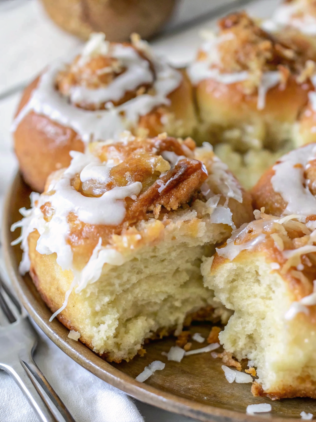 Finished Ultimate Coconut Cinnamon Rolls with cream cheese frosting and toasted coconut garnish on white serving plate