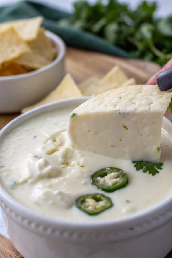 Finished queso blanco in a ceramic bowl garnished with diced tomatoes and jalapeños, served with colorful tortilla chips