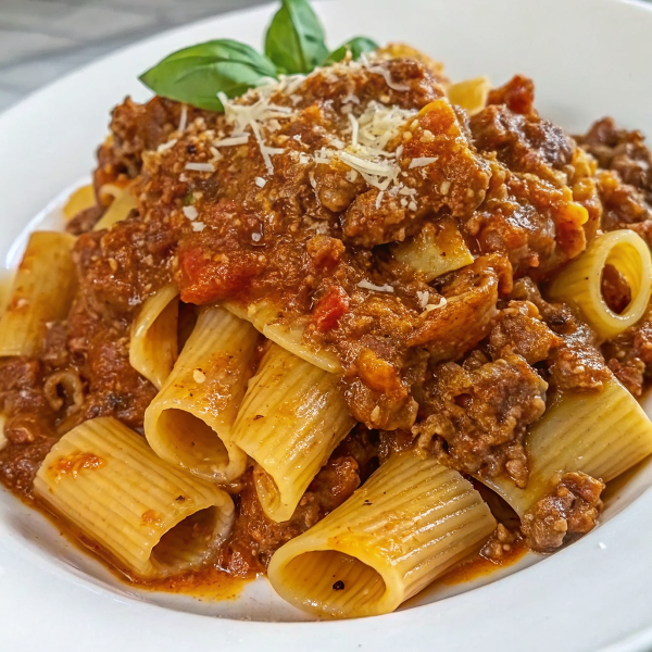 A steaming bowl of slow cooked shredded beef ragu pasta garnished with fresh parmesan and parsley, served with crusty bread