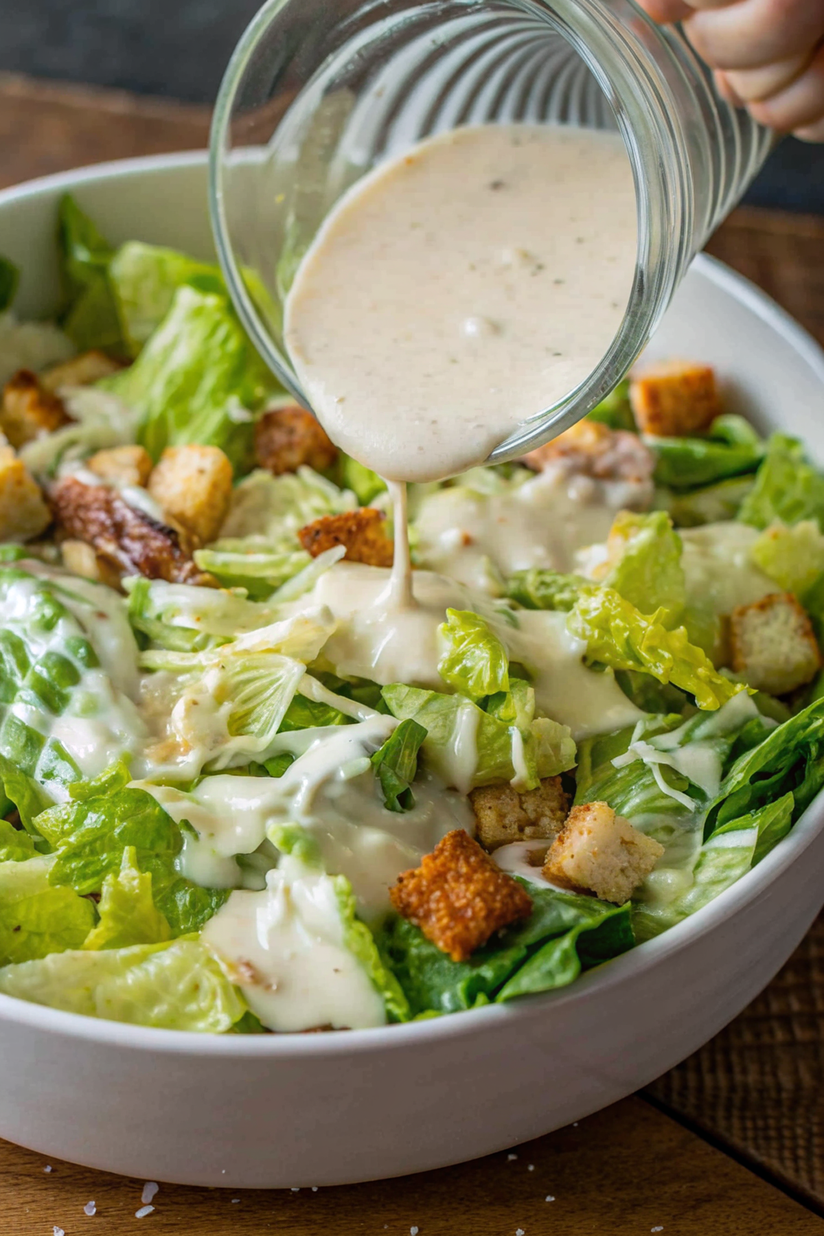 Beautiful finished homemade Caesar dressing in a glass bowl with fresh herbs and parmesan garnish