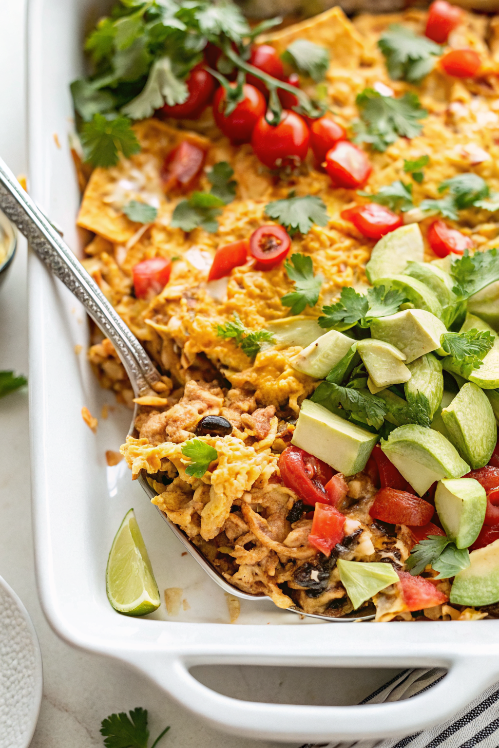 Beautifully plated Easy Chicken Taco Casserole with golden corn chip topping, garnished with fresh cilantro and lime wedges on an elegant white plate