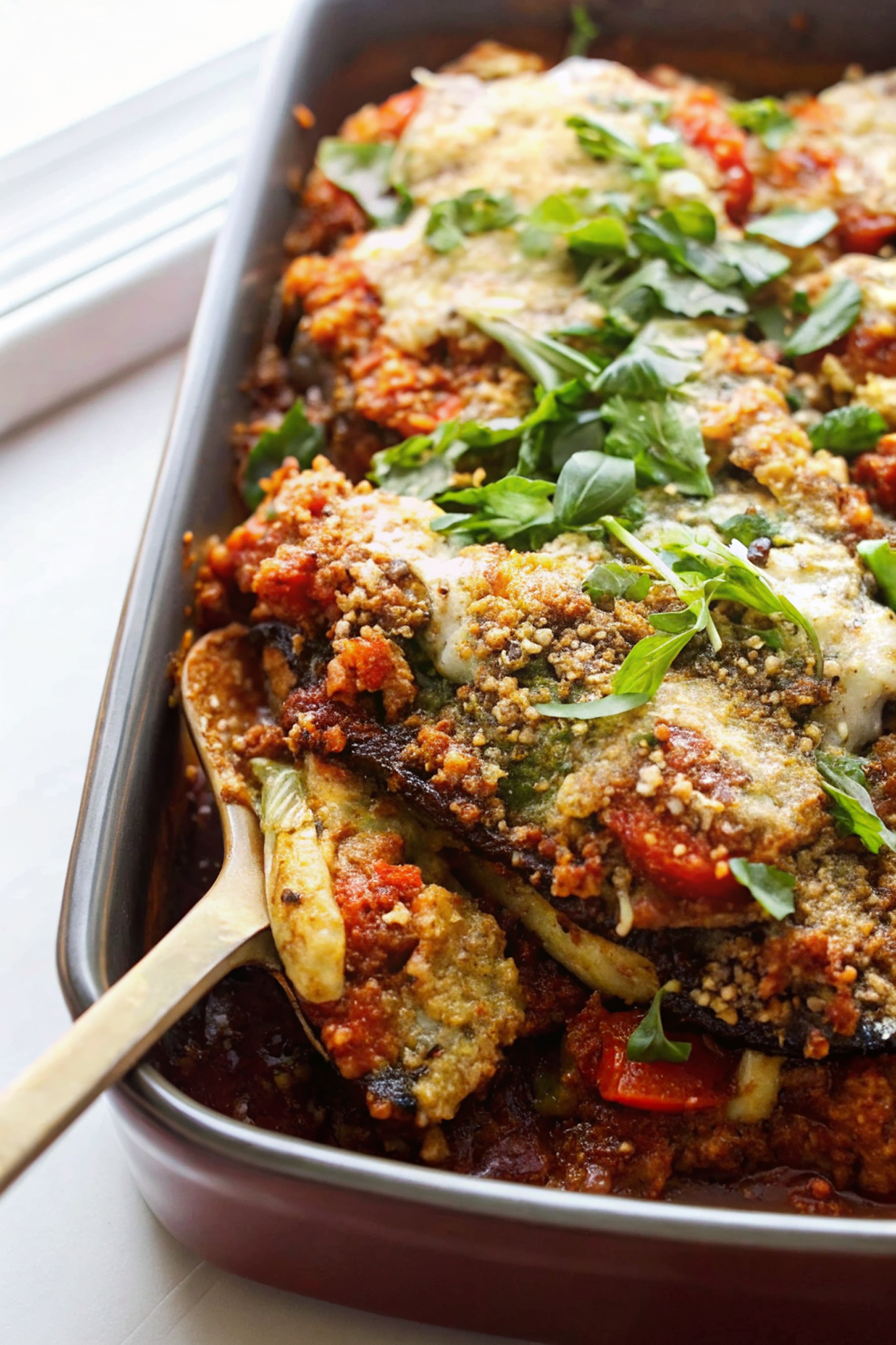 Beautiful finished vegan eggplant parmesan with golden brown top, visible layers, and fresh basil garnish on a white plate
