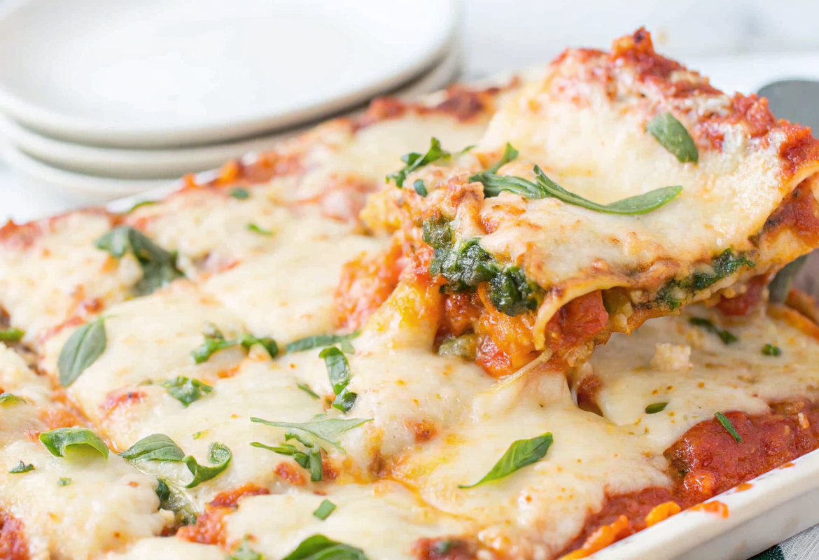 Perfectly baked Spring Vegetable Lasagna slice on a white plate showing distinct layers of pasta, creamy ricotta, and colorful vegetables with melted cheese on top