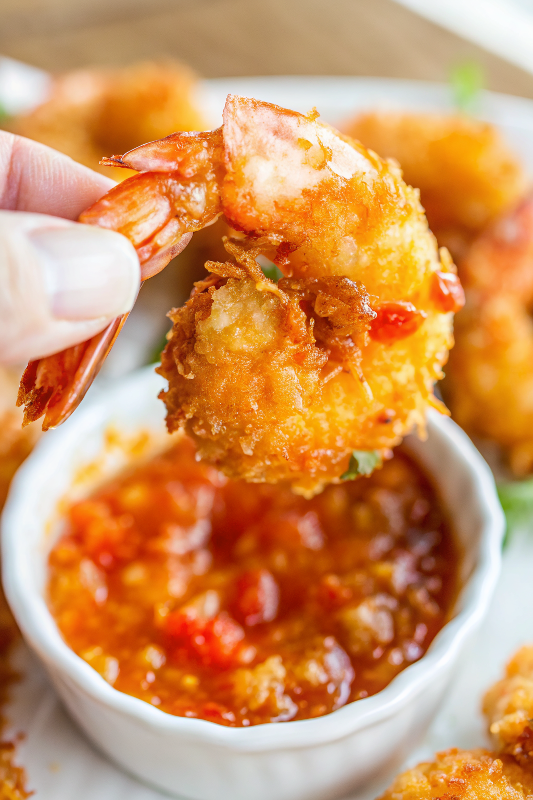Beautifully plated coconut shrimp with golden brown coating arranged on white plate with sweet chili sauce and lime garnish