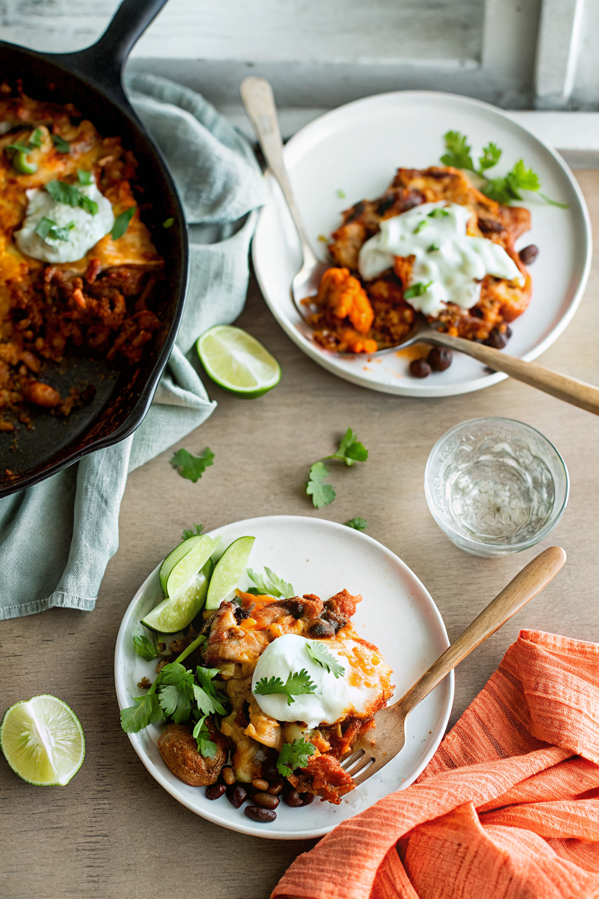 Final plated One-Pan Vegetarian Enchilada Skillet with Sweet Potatoes and Black Beans garnished with fresh cilantro, lime wedges and sour cream