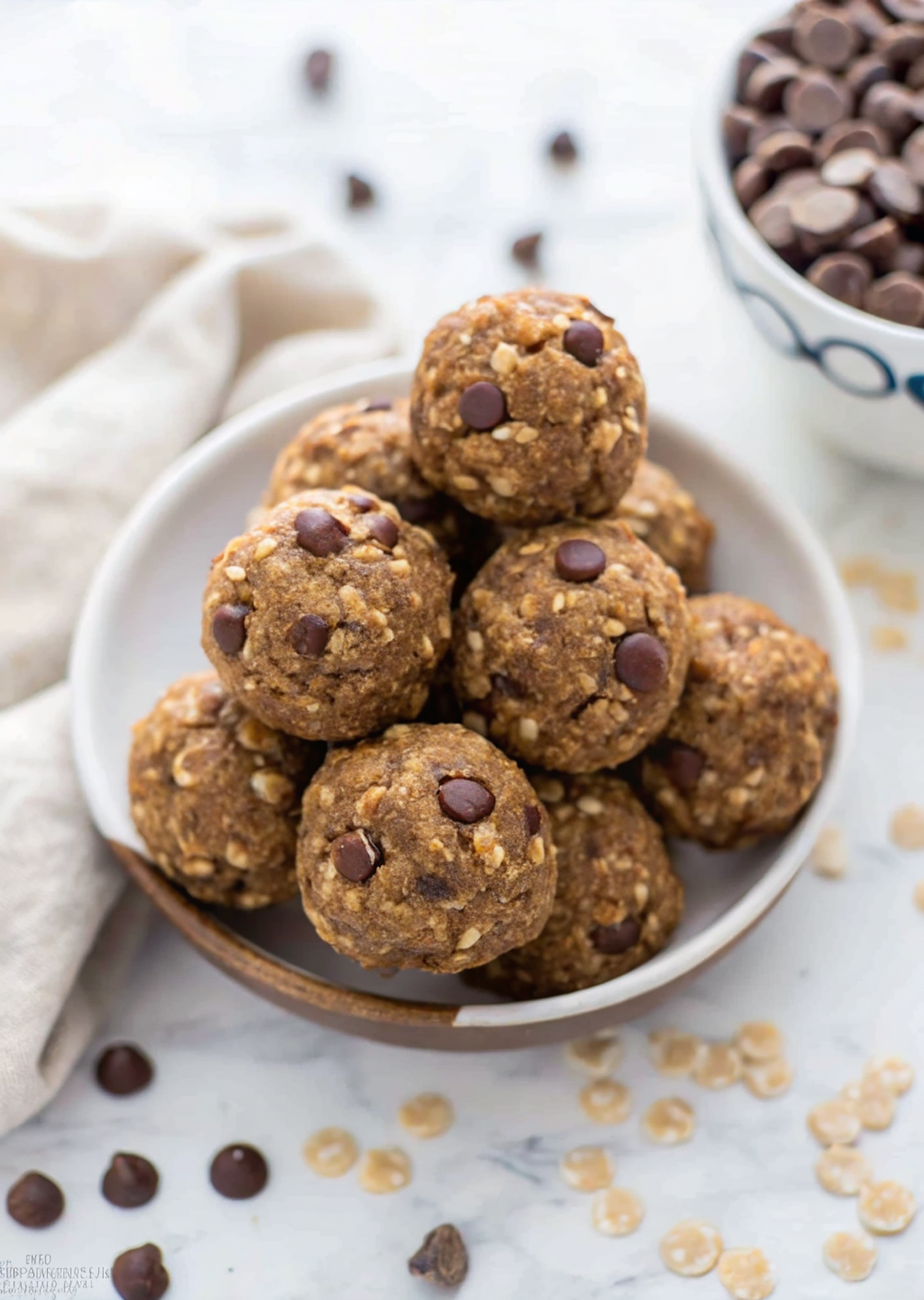 Beautiful finished no bake chocolate peanut butter energy bites arranged on a white plate with scattered oats and chocolate chips, showcasing their perfect round shape and appetizing texture