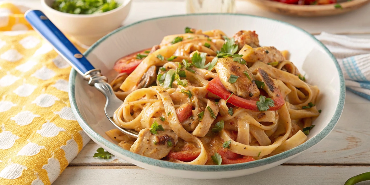 Final plated Cajun Chicken Pasta in a white bowl, garnished with fresh parsley, showing the creamy sauce coating the fettuccine with colorful vegetables and perfectly seasoned chicken pieces