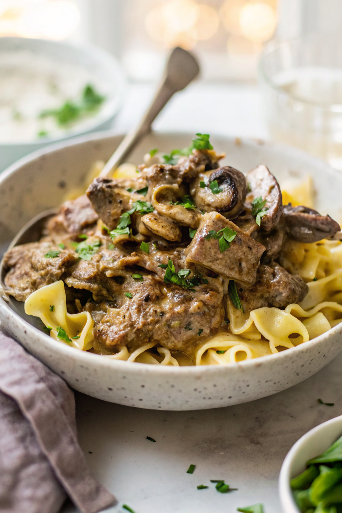 A beautiful bowl of finished slow cooker beef stroganoff with egg noodles, garnished with fresh herbs and served alongside dinner rolls