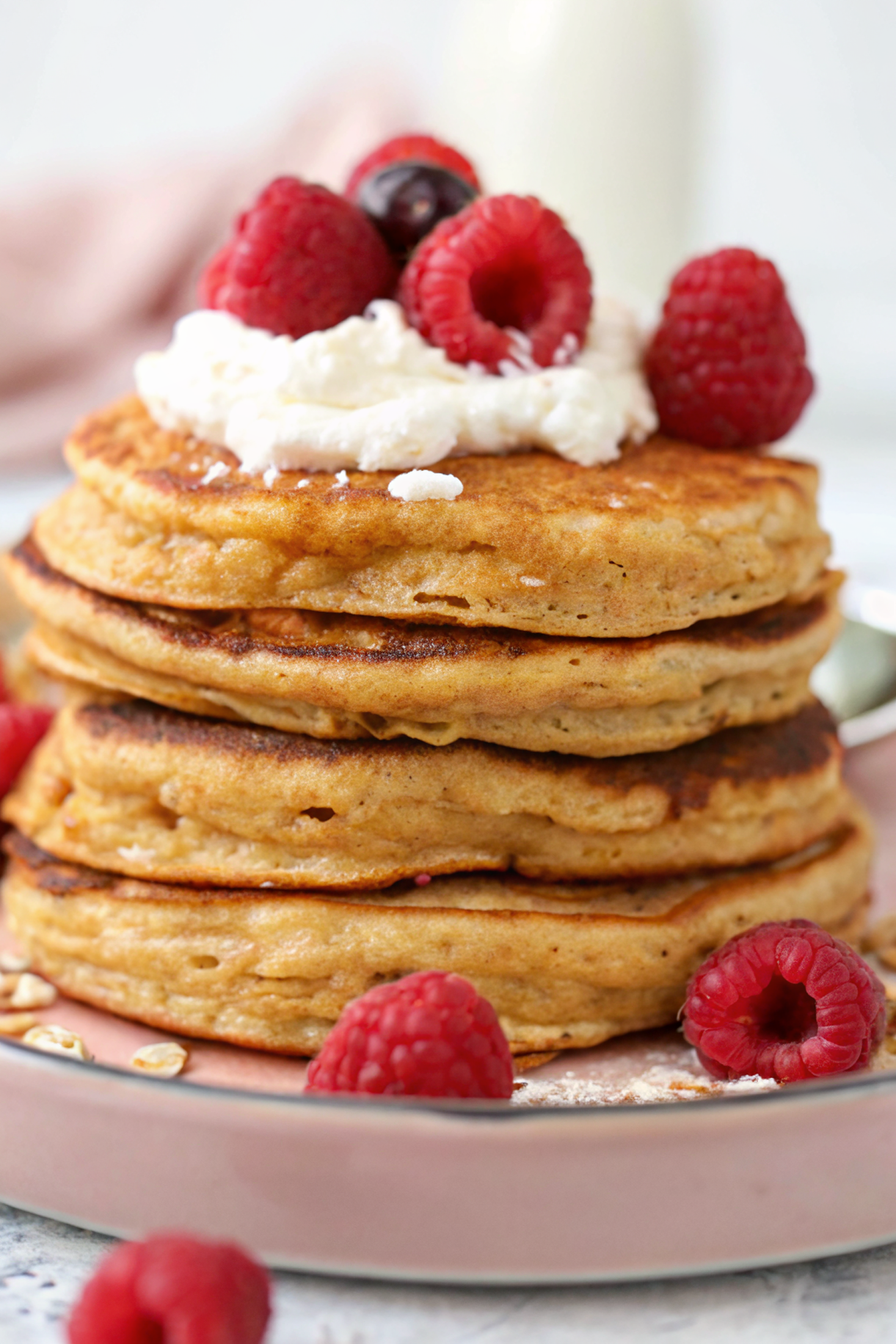 Stack of golden fluffy Greek yogurt protein pancakes with oat flour topped with fresh berries and maple syrup