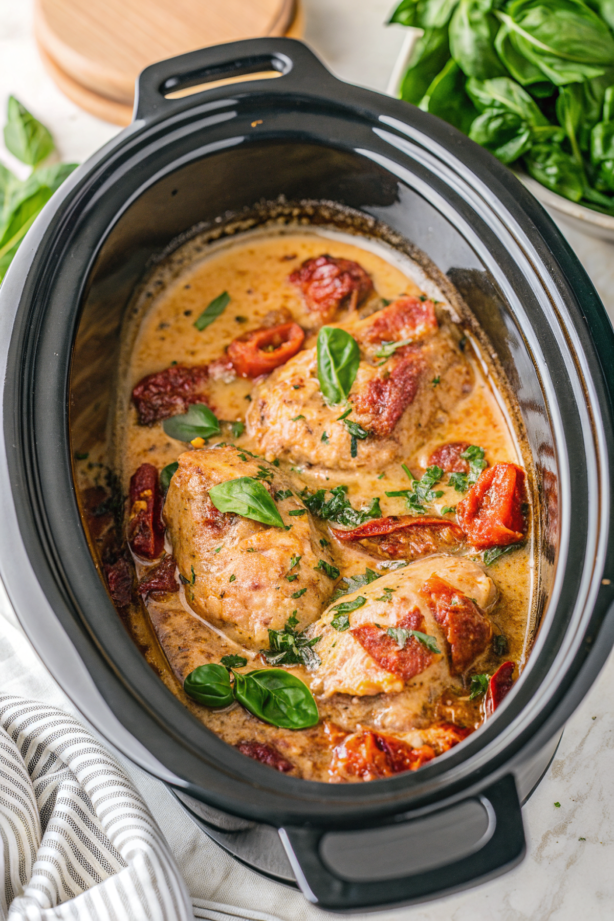 Finished Slow Cooker Tuscan Chicken served over rice with fresh basil garnish, showing creamy sauce and tender chicken in an elegant white bowl
