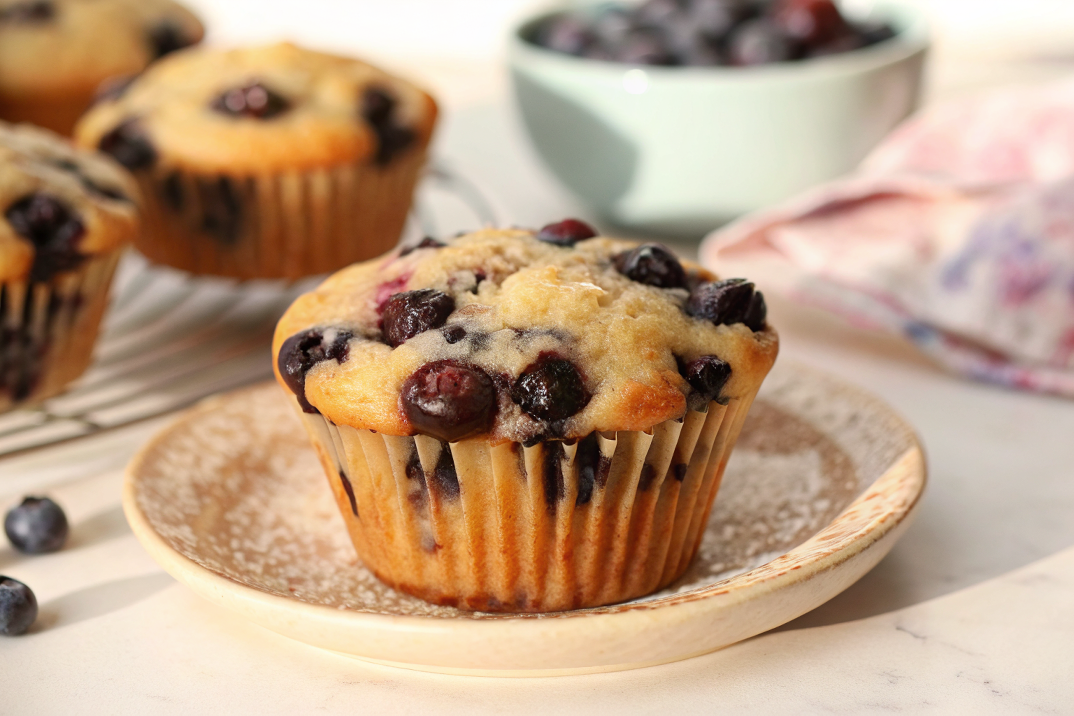 Beautiful finished Fluffy One-Bowl Blueberry Greek Yogurt Muffins with golden tops and visible blueberry bursts, arranged on a rustic wooden board